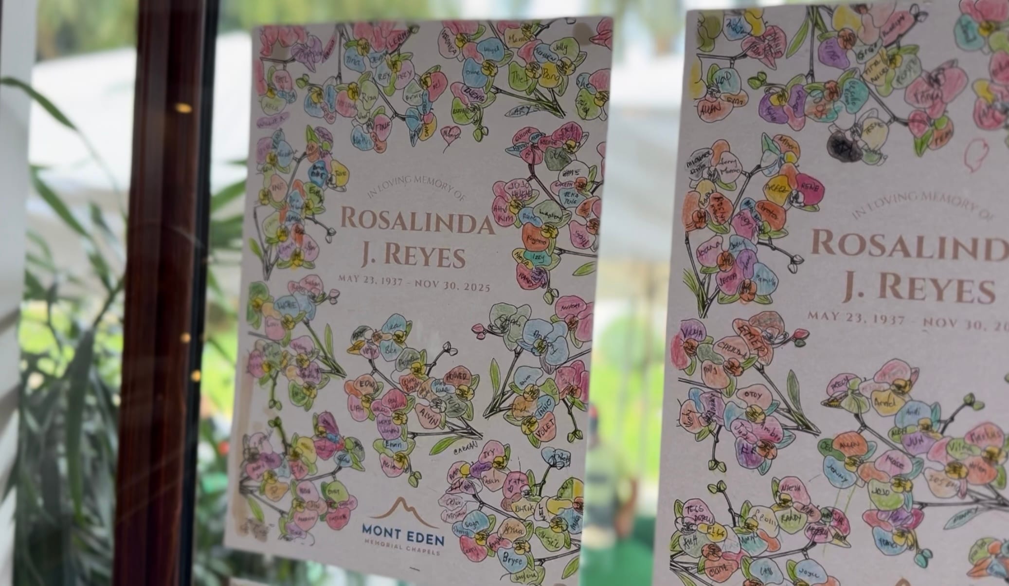 Two printed memorial cards with a floral wreath design where guests have signed their names on individual pastel-coloured petals.